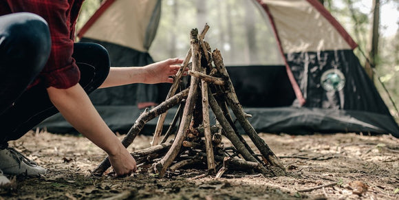 Man starting to build a campfire infront of a pitched tent.