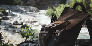 Leather backpack with water bottle sitting next to a creek.